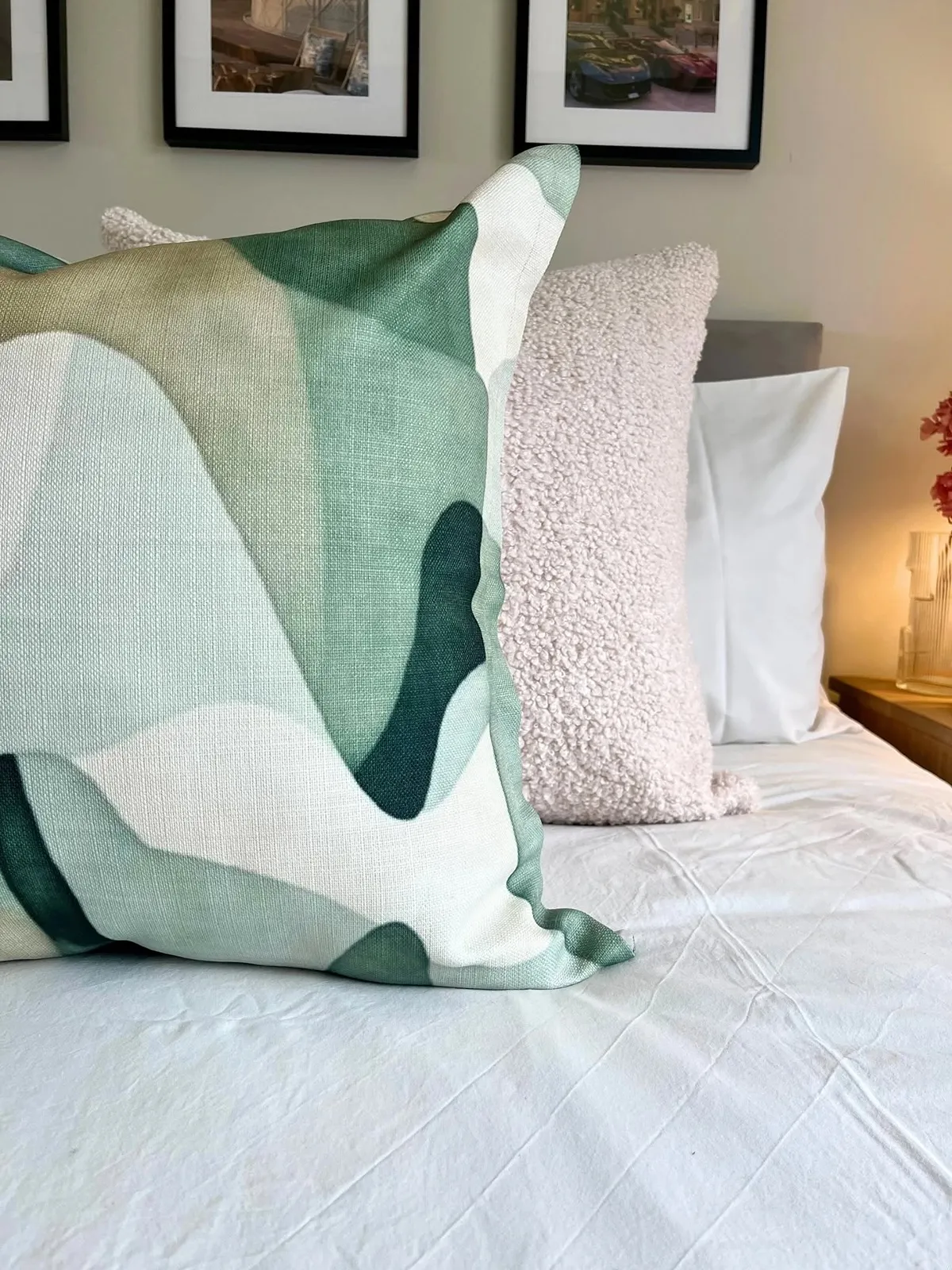A sage green abstract-print scatter cushion on a white bed, with a cream bouclé cushion behind it