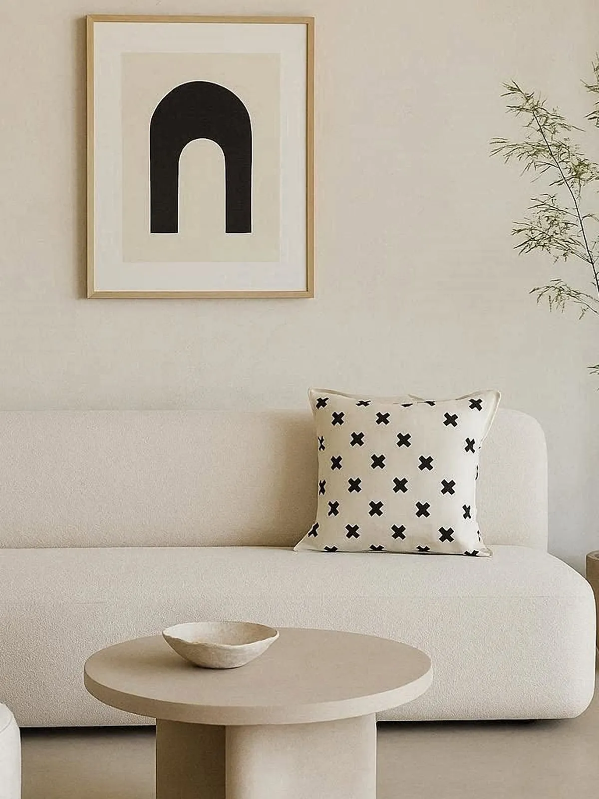 A cream sofa with a black cross-print scatter cushion, beneath a framed arch print