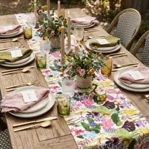 Botanical table runner on an outdoor wooden table set with plates, candles and fresh flowers